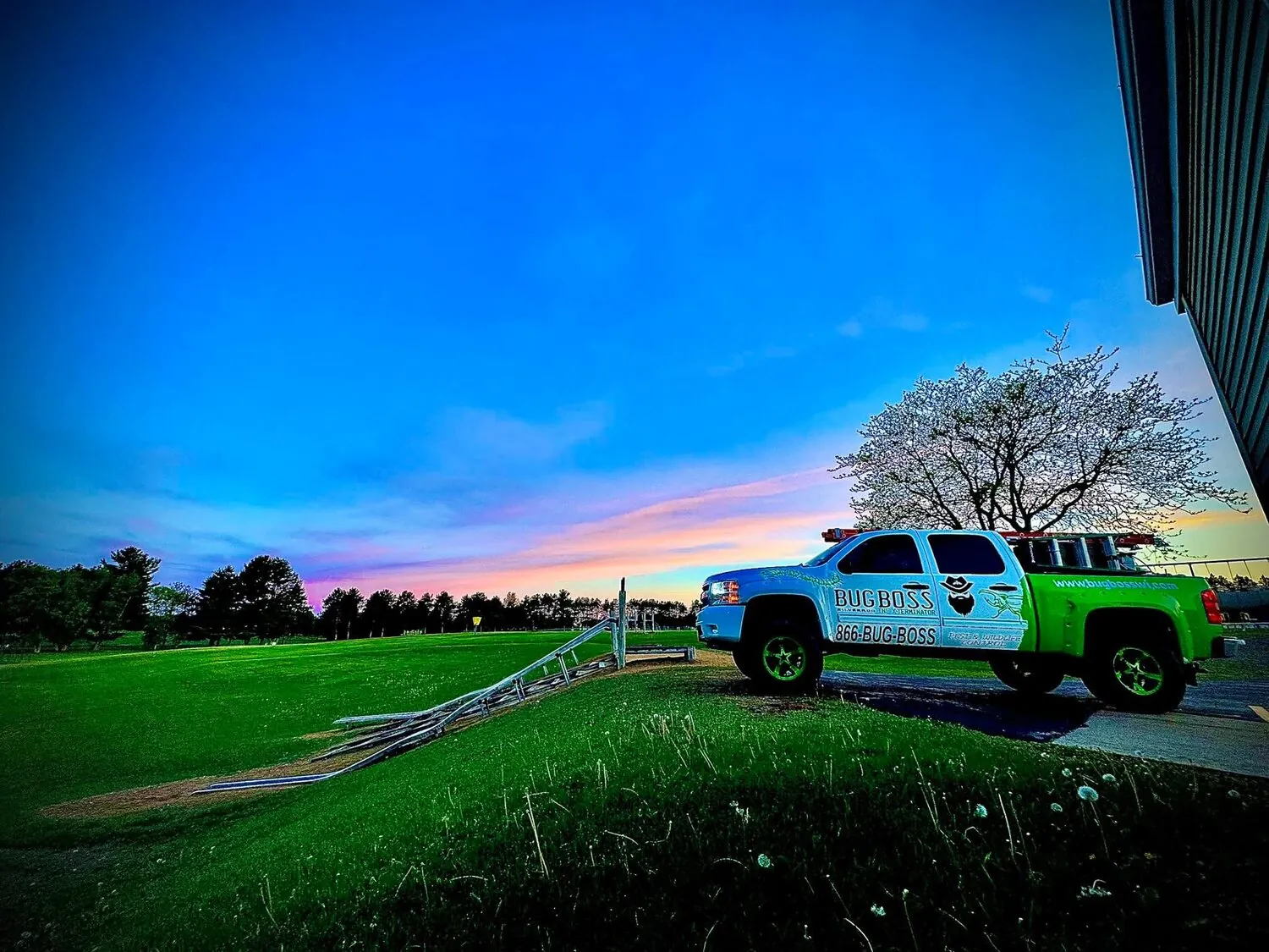 The BugBoss pest and wildlife control truck parked at dusk beside a rural Wisconsin field with ladders on the rack
